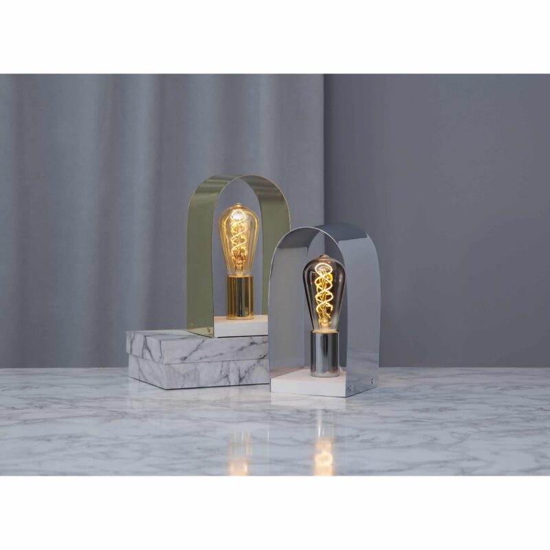 Zwei Tischlampen stehen auf einer Marmoroberfläche, jede mit einem gewölbten Metallrahmen – eine goldene und eine silberne –, in dem eine dimmbare LED-Kolbenbirne (3,2 W, 2100 K, Bernstein) steckt. Ein grauer Vorhang dient als Hintergrund.