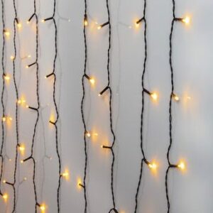 Lichtervorhang - Glimmer von Licht Factory hängt vertikal an einer schlichten Wand und strahlt mit warmen gelben Lichtern einen gemütlichen, funkelnden Effekt aus. Die Lichter sind gleichmäßig entlang dunkler Drähte verteilt und sorgen für ein sanftes Leuchten.