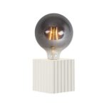 Der Leuchtenfuß - Riffle von Licht Factory verfügt über eine moderne Glühbirne mit sichtbarem Glühfaden, die auf einem strukturierten, weißen, rechteckigen Sockel sitzt. Das getönte Glas verleiht ihm ein elegantes und modernes Aussehen.