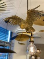 Die Pendelleuchte - Hedwig ist eine dekorative Pendelleuchte, die als fliegender Vogel mit elegant ausgebreiteten Flügeln gestaltet ist. Der Vogelkopf verbindet sich nahtlos mit einer Glühbirne und bietet ein einzigartiges Design, das sich perfekt für Innenräume eignet, die mit ähnlichen Leuchten geschmückt sind, die im Hintergrund wunderschön beleuchtet sind.