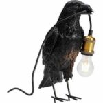 Die Tischleuchte - Black Crow verfügt über ein schwarzes Krähendesign mit einer Glühbirne im Schnabel, die von einer messingfarbenen Fassung gehalten wird.