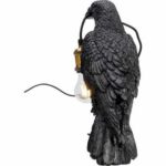 Die Tischleuchte – Black Crow ist eine detailreiche dekorative Skulptur eines schwarzen Raben mit realistischer Federtextur, der eine brennende Glühbirne in seinem Schnabel hält, die an einem schwarzen Kabel befestigt ist.