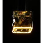 Ein leuchtendes Leuchtmittel Floatlight IceCube 6W dimmbar rauch 12,5cm hängt vor einem schwarzen Hintergrund und strahlt ein warmes, einladendes Licht aus. Seine strukturierte, reflektierende Oberfläche verleiht der Szene Tiefe und Eleganz.