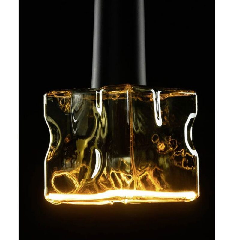 Eine Nahaufnahme zeigt das Leuchtmittel - Floatlight IceCube 6W dimmbar rauch 12,5cm, ein durchscheinendes Objekt aus Bernsteinglas mit strukturierten Oberflächen. Von unten vor einem schwarzen Hintergrund beleuchtet, hebt es warme Reflexionen und Schatten auf seinen Kurven und Kanten hervor.