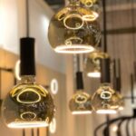 Die Pendelleuchten Floatlight Globe von Leuchtmittel mit dimmbaren 4W-Goldglasschirmen (Ø15cm) hängen versetzt. Ihr warmes, bernsteinfarbenes Leuchten erzeugt vor einem sanft verschwommenen Hintergrund eine gemütliche und elegante Atmosphäre.