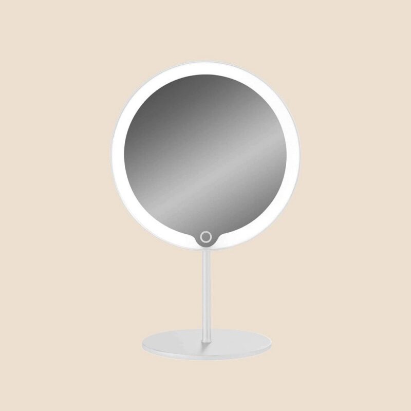 Der Kosmetikspiegel - Ringlight, ein runder Tischspiegel mit beleuchtetem Rand, wird auf einem runden Sockel vor einem beigen Hintergrund präsentiert.