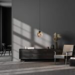 Ein modernes Wohnzimmer zeichnet sich durch dunkelgraue Wände und minimalistische Möbel aus. Auf einem eleganten Sideboard sind Dekoartikel und Pampasgras ausgestellt. Darüber hängt die stilvolle Pendelleuchte - Bubble 1er (M) und verbreitet ein sanftes Licht, während daneben ein heller Stuhl steht. Sonnenlicht fällt durch und erzeugt Schatten am Fenster.