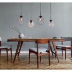 In einem modernen Esszimmer steht ein Holztisch mit vier Stühlen und grauen Kissen, geschmückt mit einer Vase mit weißen Blumen. Darüber erhellt die *Pendelleuchte - Bubble 4er* mit Glasschirmen den Raum. Der Fischgrät-Holzboden ergänzt die elegant grau gestrichene Wand.