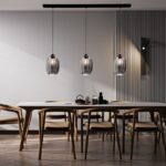 Das moderne Esszimmer verfügt über einen langen weißen Tisch mit Holzstühlen, der von drei Pendelleuchten – Salva 3er aus Glas beleuchtet wird. Die grauen Wände haben auf der rechten Seite eine strukturierte Platte und der Boden weist ein stilvolles Fischgrätenmuster auf.