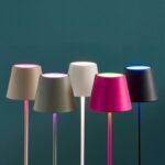 Fünf Akku LED Tischleuchten - Bunte RGB-Lampen mit konischen Schirmen stehen vor einem blaugrünen Hintergrund. Die Schirme in Erdtönen, Rosa und Schwarz leuchten in Rosa-, Grün-, Blau- und Weißtönen und erzeugen darunter einen lebendigen Farbverlaufseffekt.