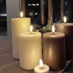 Eine Gruppe von brennenden LED Kerzen - Authentic - mocca Kerzen, in verschiedenen Größen und Farben wie Mokka, sind auf einem Tisch arrangiert. Der schwach beleuchtete Hintergrund suggeriert eine gemütliche oder intime Atmosphäre.