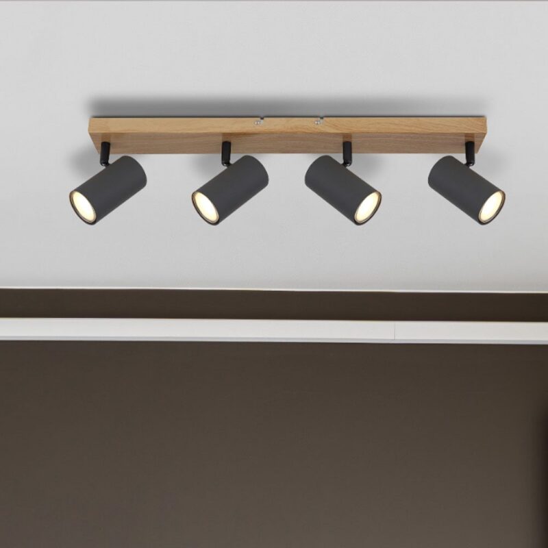 Der Deckenstrahler – Dari 4er verfügt über einen rechteckigen Holzsockel und vier verstellbare schwarze zylindrische Lichter, die an einer weißen Decke über einer dunkelbraunen Wand montiert sind.