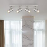 Der Deckenstrahler – Dari 4er, eine moderne Deckenleuchte mit vier verstellbaren Strahlern, wertet einen Raum mit großen Fenstern, transparenten Vorhängen und einer Akzentsäule aus Marmor auf.