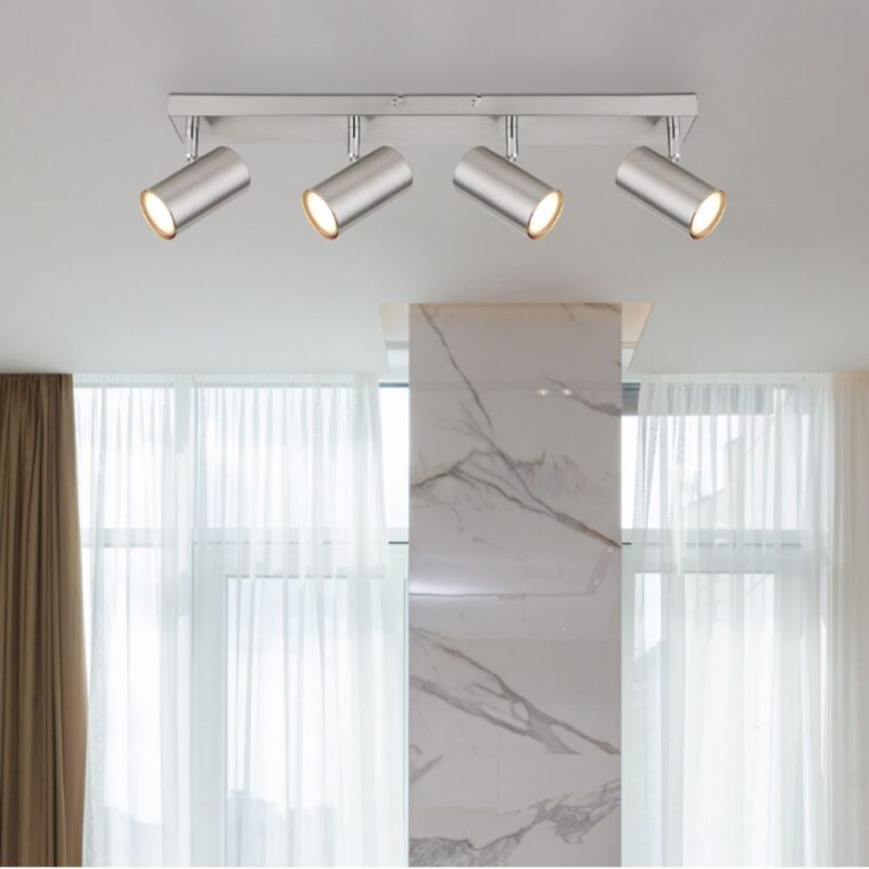 Der Deckenstrahler – Dari 4er, eine moderne Deckenleuchte mit vier verstellbaren Strahlern, wertet einen Raum mit großen Fenstern, transparenten Vorhängen und einer Akzentsäule aus Marmor auf.