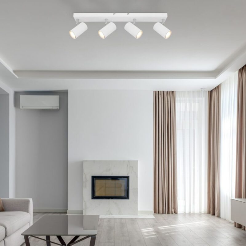 Ein modernes Wohnzimmer ist mit einem Dari 4er Deckenstrahler, beigen Vorhängen und einem grauen Sofa ausgestattet. Hellgraue Wände ergänzen die wandmontierte Klimaanlage über dem weißen Marmorkamin, während große Fenster den Raum mit natürlichem Licht durchfluten und so für eine einladende Atmosphäre sorgen.