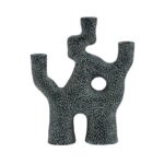 Der Kerzenhalter - Trio ist eine schwarze Keramikskulptur mit einer strukturierten, abstrakten Form, die an einen Baum oder eine Koralle erinnert. Er fungiert als einzigartiger Kerzenhalter mit drei nach oben gerichteten Zweigen, einer zentralen runden Öffnung und ist mit kleinen weißen Flecken in einem faszinierenden gepunkteten Muster verziert.