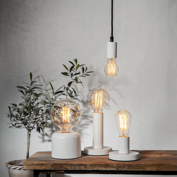 Auf einem Holztisch stehen drei moderne Lampen mit Leuchtmittel - Globe 3,8 W 1800 K dimmbar Ø12,5 cm Glühbirnen in verschiedenen Formen und Größen. Eine hängende Glühbirne sorgt für Tiefe, während links eine Topfpflanze mit schmalen Blättern vor einer schlichten Wand steht.