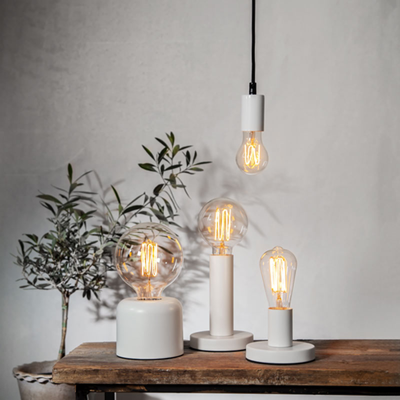 Auf einem Holztisch stehen drei moderne Lampen mit Leuchtmittel - Globe 3,8 W 1800 K dimmbar Ø12,5 cm Glühbirnen in verschiedenen Formen und Größen. Eine hängende Glühbirne sorgt für Tiefe, während links eine Topfpflanze mit schmalen Blättern vor einer schlichten Wand steht. Auf einem Holztisch stehen drei moderne Lampen mit Leuchtmittel - Globe 3,8 W 1800 K dimmbar Ø12,5 cm Glühbirnen in verschiedenen Formen und Größen. Eine hängende Glühbirne sorgt für Tiefe, während links eine Topfpflanze mit schmalen Blättern vor einer schlichten Wand steht.