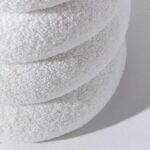 Nahaufnahme von drei gestapelten, runden weißen Handtüchern mit weicher, strukturierter Optik, die sanft wie der Sitzpouf – Wolke auf einer hellgrauen Oberfläche ruhen und einen Schatten aufwerfen.