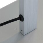 Eine Nahaufnahme zeigt ein schwarzes Kabel, das durch eine kleine Gummitülle in den glatten, metallisch silbernen Rahmen einer Tischleuchte – Leve eintritt und auf einer hellen, reflektierenden Oberfläche ruht.