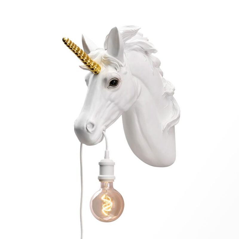 Die Wandleuchte - Einhorn, eine weiße Wandskulptur, hat ein goldenes Horn und eine wallende Mähne, in deren offenem Mund eine leuchtende Glühbirne steckt. Ihr warmes Licht bildet einen eleganten Kontrast zum schlichten weißen Hintergrund.