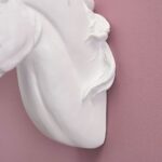 Nahaufnahme einer Pferdekopfskulptur aus weißem Marmor mit detailreicher Mähne und Hals, beleuchtet von der eleganten Unicorn Wandleuchte. Das Stück sticht vor einer glatten pastellrosa Wand hervor.