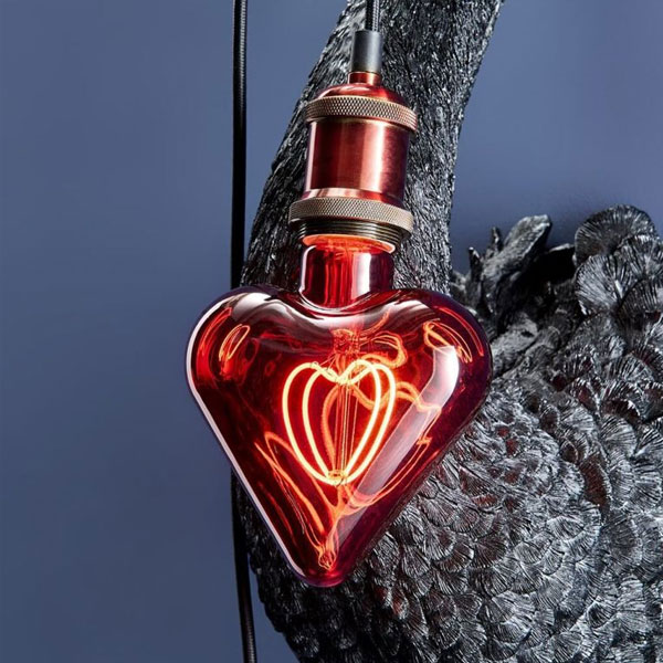 Eine Leuchtmittel-Glühbirne (Red Heart) mit glühendem Glühfaden hängt vor einer schwarzen Schwanenskulptur vor einem blauen Hintergrund.