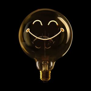 Die Statement-Glühbirne „Smiley Zufrieden“ mit einem Glühfaden in Form von Augen und einem Lächeln leuchtet fröhlich vor dem schwarzen Hintergrund.