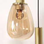 Die Pendelleuchte - Lucy 2.0 - 9er verfügt über eine Glühlampe im Vintage-Stil in einem transparenten Gehäuse mit bernsteinfarbenem Farbton, goldenen Akzenten und einem schwarzen Kabel. Sie strahlt ein warmes Licht aus, das den eleganten Look der Lampe unterstreicht.