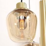 Nahaufnahme der Pendelleuchte Lucy 2.0 - 9er im Vintage-Stil mit freiliegender Glühlampe aus transparentem, bernsteinfarbenem Glas. Die Leuchte hat metallische Akzente und strahlt ein warmes Licht aus.