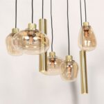 Die Pendelleuchte - Lucy 2.0 - 9er besteht aus einer Reihe moderner Pendelleuchten mit Glas- und Messingfassungen in verschiedenen Formen. Die Glühbirnen strahlen ein warmes Licht aus und unterstreichen die elegante, zeitgenössische Ästhetik vor einem schlichten, hellen Hintergrund.