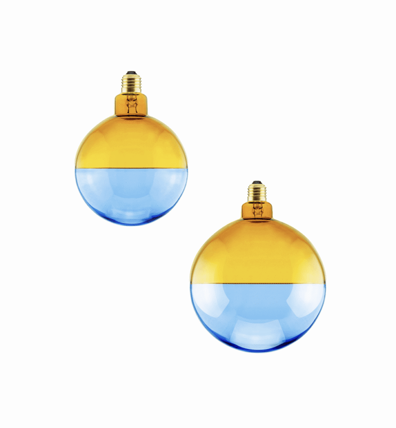 Das LED-Leuchtmittel Illusion verfügt über zwei kugelförmige Glühbirnen mit einem einzigartigen halb gelben, halb blauen Design, die auf einem weißen Hintergrund angeordnet und mit einem eleganten goldfarbenen Sockel geschmückt sind.