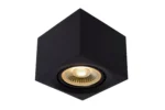 Der Deckenstrahler - Blacky ist eine moderne, minimalistische schwarze Deckenleuchte in Würfelform mit einer runden, versenkten Glühbirne, die ein warmes, gelbes Licht ausstrahlt. Sie hat scharfe Kanten und eine glatte Oberfläche.