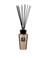 Der Diffusor Raumduft – Exklusives Cyrium ist goldfarben mit schwarzen Rattanstäbchen und einem schwarzen Etikett mit goldenen Details, alles auf einem schlichten weißen Hintergrund.