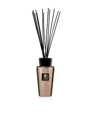 Der Diffusor Raumduft – Exklusives Cyrium ist goldfarben mit schwarzen Rattanstäbchen und einem schwarzen Etikett mit goldenen Details, alles auf einem schlichten weißen Hintergrund.