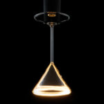Das LED-Leuchtmittel - Cocktails von Licht Factory hängt kopfüber und strahlt aus seinem Sockel ein warmes gelbes Licht aus. Das leuchtende Weinglas erzeugt vor dem dunklen Hintergrund einen sanften Halo-Effekt.