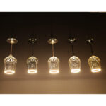 Eine Reihe von sechs LED-Leuchtmitteln - Cocktails-Pendelleuchten von Licht Factory erhellt die dunkle Decke, jede mit transparenten Glasschirmen. Das warme Leuchten unterstreicht die dekorative Eleganz, die dem Design jeder Leuchte innewohnt.