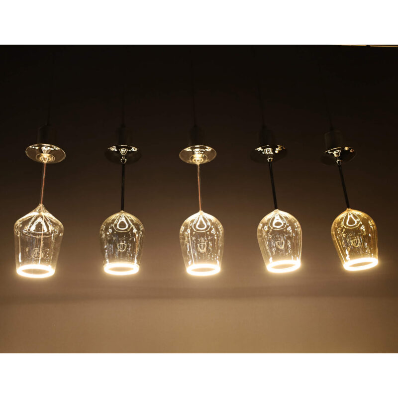 Eine Reihe von sechs LED-Leuchtmitteln - Cocktails-Pendelleuchten von Licht Factory erhellt die dunkle Decke, jede mit transparenten Glasschirmen. Das warme Leuchten unterstreicht die dekorative Eleganz, die dem Design jeder Leuchte innewohnt.