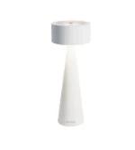 Die Tischleuchte - Elody ist eine moderne weiße Tischlampe mit zylindrischer Oberseite und kegelförmigem Sockel, die weiches, nach unten gerichtetes Licht abgibt. Ihr minimalistisches Design und die schlanke und glatte Oberfläche machen sie perfekt für eine moderne Einrichtung.