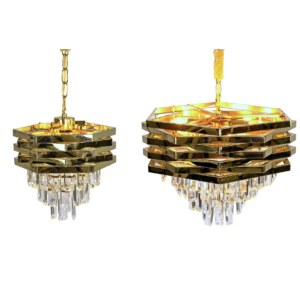 Zwei Kronleuchter aus Krystal Gold haben ein sechseckiges Design mit mehrschichtigen Metallringen und herabhängenden Kristallanhängern, die an Goldketten hängen und warmes Licht abgeben. Der Kronleuchter links ist etwas größer. Verfügbar ab Woche 6, 2025.