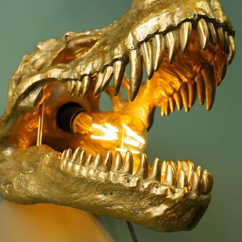 Nahaufnahme von dem maul der Dino wand leuchte die leuchte ist eingeschaltet und ist gold der Hintergrund ist türkis grün