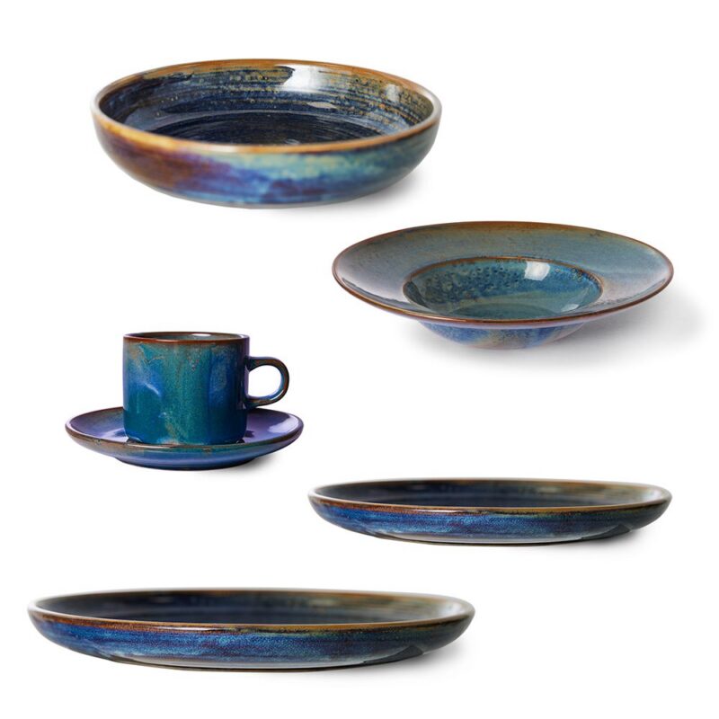 Die Kollektion „Chef Ceramics – Rustic Blue“ von HK Living umfasst Keramikgeschirr mit einer tiefblauen und braunen Glasur. Sie umfasst einen Becher mit Untertasse, eine flache Schüssel, eine tiefe Schüssel und zwei unterschiedlich große Teller, die alle unregelmäßige künstlerische Muster aufweisen.