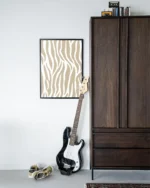 Eine schwarze E-Bassgitarre lehnt an einem Holzschrank. Daneben liegen abgetragene Turnschuhe auf dem Boden. Darüber hängt ein gerahmtes Wandbild – Savanna Beige mit beige-weißem Muster, während Bücher und eine Kamera auf dem Schrank die Kreativität anregen.