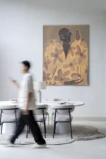 Eine verschwommene Person geht durch einen modernen Essbereich mit einem runden Tisch und Stühlen. Ein großes, mit Blumen geschmücktes Wandbild – Twins verleiht der Wand Faszination, während das in Savannenbeige gehaltene Dekor eine elegante Lampe umfasst, die die ruhige Atmosphäre verstärkt.